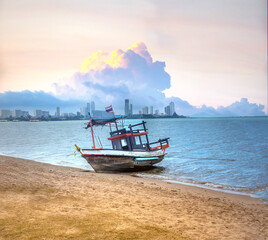 Obraz premium An idle fishing boat on the sands of Krathing Lai beach with the skyline of the city of Pattaya in the background, Thailand