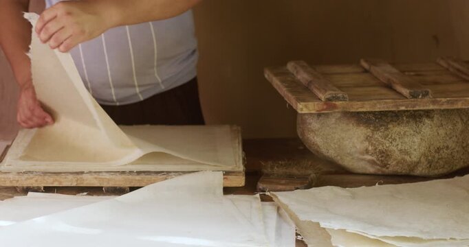 Fresh handmade paper sheets placed on a wooden press and drying surface inside a traditional workshop. This scene illustrates the manual papermaking process using natural fibers and simple tools.