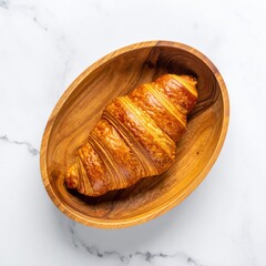 Golden-brown croissant in a wooden bowl on a white marble surface