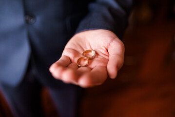 On a man's palm are two wedding rings. The groom holds the rings. Wedding tradition. Gold rings lie on a man's palm.