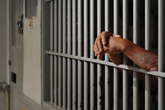 Close up view of hands behind bars in a prison cell, symbolizing incarceration and the criminal justice system.