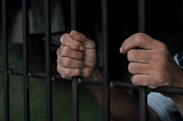 Obraz premium Close up view of hands behind bars in a prison cell, symbolizing incarceration and the criminal justice system.