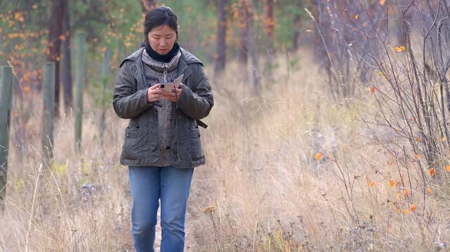 Chinese woman looking at cell phone while walking in the forest on an autumn day