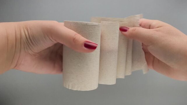 Female hands tear a piece of toilet paper from a roll on a gray background. Secondary cellulose. Disposable Toilet Paper