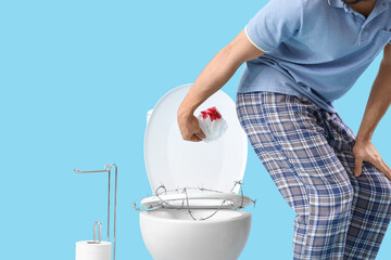 Young man with bloody paper and toilet bowl in barbed wire on blue background. Hemorrhoids concept