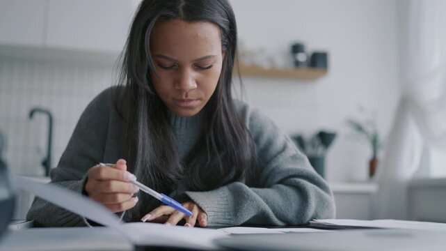 Concentrated lady checking papers and notes in pad, home workplace of freelancer . Female student learning and doing homework, portrait of charming african american woman, knowledge and education
