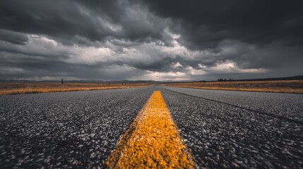 A straight, asphalt road stretches toward a distant horizon under a dramatic, overcast sky, evoking a sense of journey