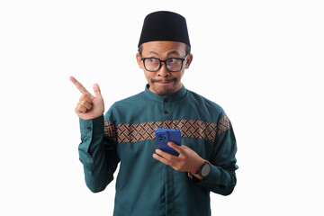 Asian Muslim man wearing a green traditional outfit and eyeglasses is pointing while holding a phone, Isolated on a white background