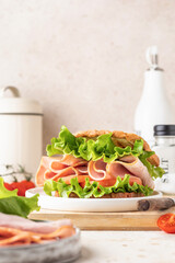 Delisious sandwich with ham lettuce tomatoes and grilled bread for breakfast on wooden board, beige kitchen table
