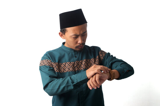 Serious Asian Muslim man checking the time on his wristwatch while waiting for iftar or suhoor before imsak during Ramadan fasting. Isolated on a white background, time management and fasting concept