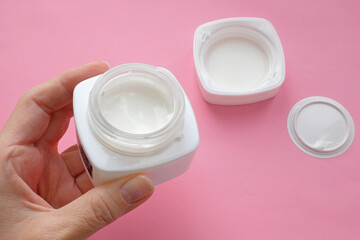 woman hands with cream cosmetic bottles on pink background, cold season hands skin protection. Top view