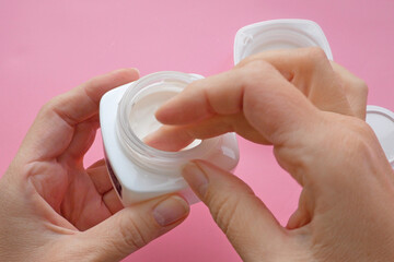 woman hands with cream cosmetic bottles on pink background, cold season hands skin protection. Top view