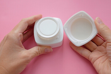 woman hands with cream cosmetic bottles on pink background, cold season hands skin protection. Top view
