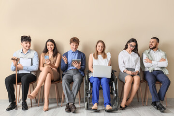 Job applicants with woman in wheelchair waiting for interview near beige wall