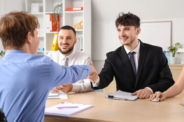 Male applicant in wheelchair with human resources commission shaking hands during job interview at office