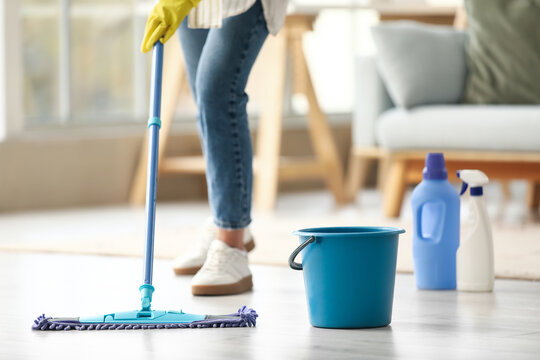Young woman with plastic bucket mopping floor at home