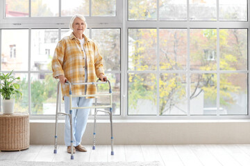 Senior woman with walker near window at home