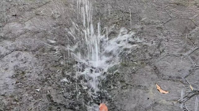 Heavy rain water pouring and splashing on wet muddy paving blocks ground with dry leaves during a storm