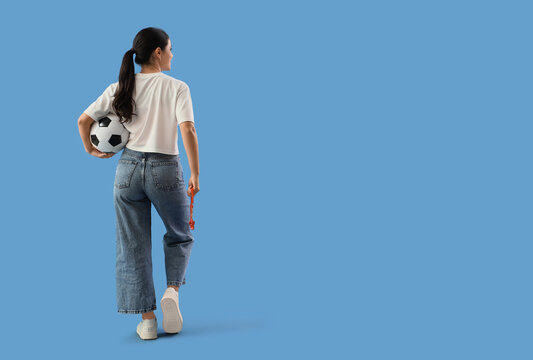 Female soccer fan with ball and whistle on blue background, back view