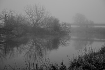 Nebel &uuml;ber dem Fluss mit B&auml;umen und einer Br&uuml;cke im Hintergrund