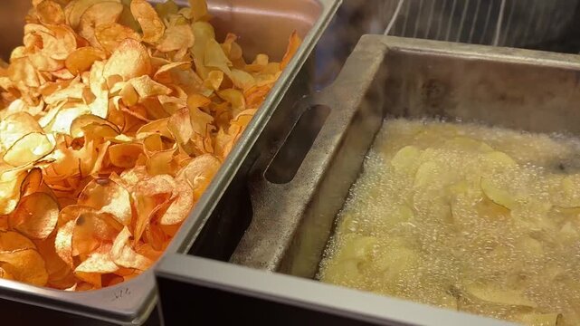 Potato chips falling from automatic dispenser onto conveyor inside modern food production facility, close up view of snack processing and distribution system.