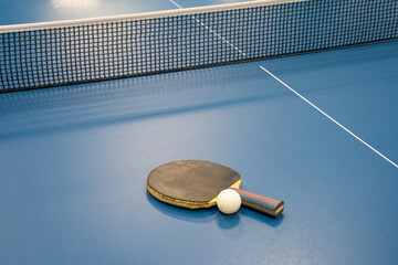 A table tennis paddle and ball on a table tennis table next to the net. Sports equipment ready for play.

