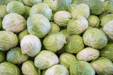 A pile of fresh cabbage heads filling the frame, showcasing natural textures and organic shapes in a simple, minimalist agricultural composition.

