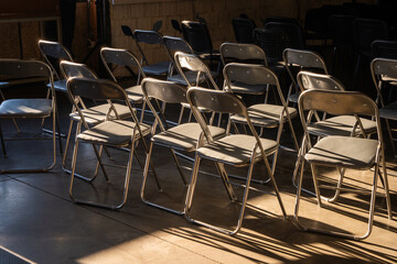A pile of unfolded chairs in an event space, empty and unused. Stacked seating equipment awaiting setup or storage.

