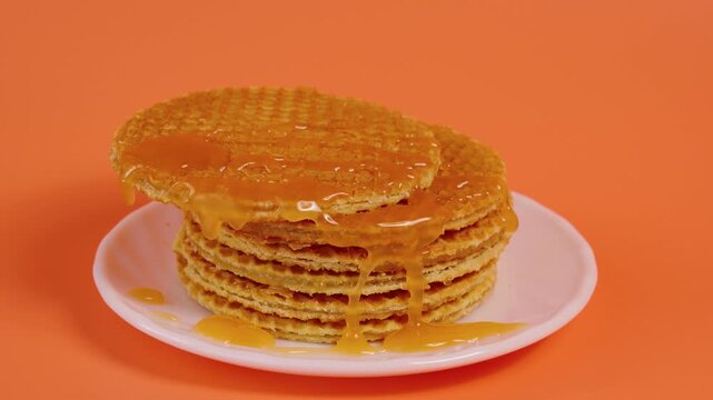 Stack of stroopwafels with caramel syrup dripping on orange background. High quality 4k footage