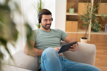 Man relaxing on sofa enjoying music and tablet