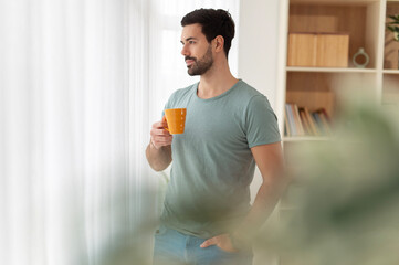 Man holding coffee looking out window daydreaming