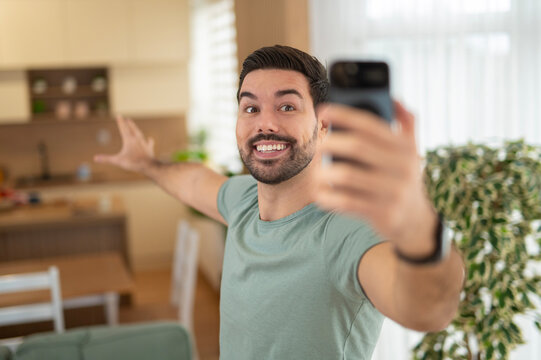 Young happy man vlogging and showing home on smartphone