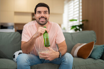 Happy man watching soccer match, drinking beer and eating popcorn