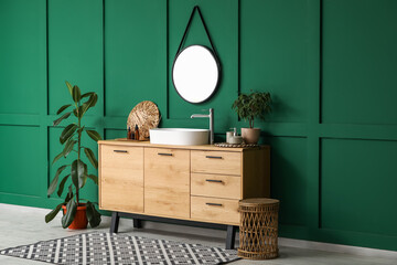 Chest of drawers with sink, bath accessories and plants near green wall in bathroom interior