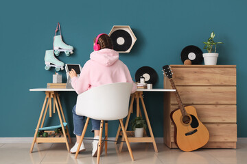 Teenage girl with headphones using tablet computer at table in room, back view