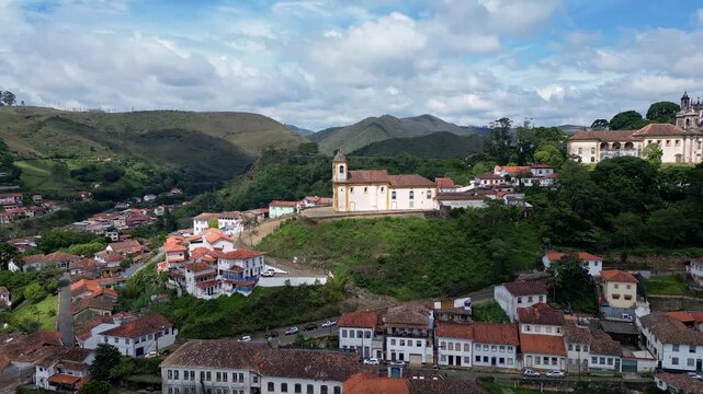 Ouro Preto, Brazil: Orbit aerial drone footage of Ouro Preto old town in Minas Gerais state of Brazil with church of Lady of Mercy under cloudy sky and lush valley in south America