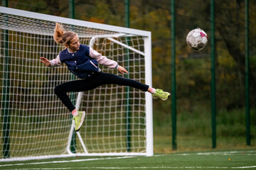 young girl jumps to kick a soccer ball away from the goal