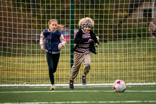 Children play football on an outdoor stadium with artificial turf.