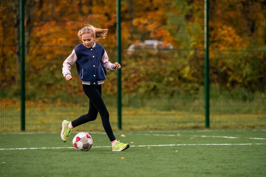 Young caucasian girl playing soccer on outdoor artificial grass field