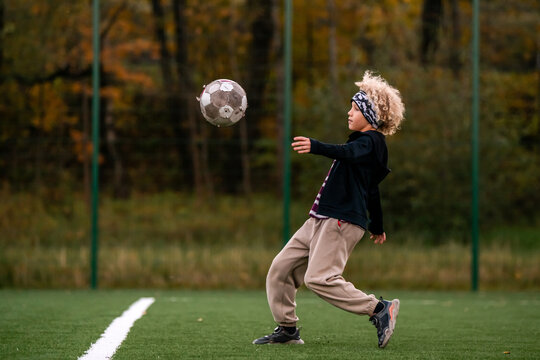 Young boy playing soccer, kicking ball on green field.
