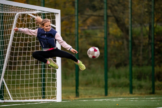 young girl jumps to kick a soccer ball away from the goal