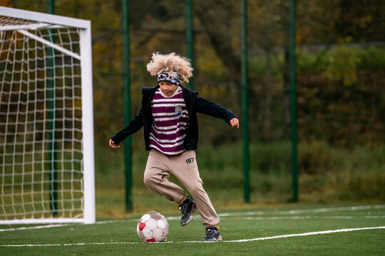 Young boy playing soccer, kicking ball on green field.