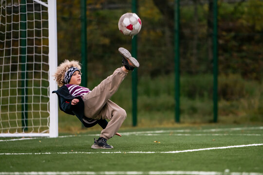 Boy kicking soccer ball in mid-air on a green football field.