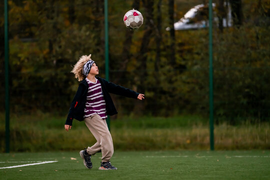Young boy playing soccer, kicking ball on green field.
