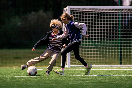 Children play football in an open stadium with artificial lighting.
