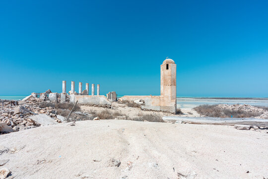 Al-Jumail, Qatar - March 18, 2025. Deserted coastal abandoned village ruins with minaret tower and columns under a bright blue sky