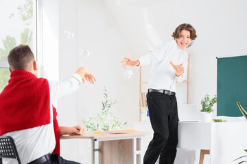 Fototapeta premium Teenage student throwing crumpled paper at classmate in classroom
