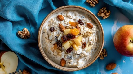 Overhead View of Oatmeal Breakfast with Fruits and Nuts in Bowl on Blue Surface Beside Apple