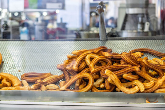 A pile of delicious, golden-brown fried dough pastries known as churros or porras behind a glass display in a street food stall.