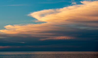 Clouds gather above the ocean during sunset while the sky is painted with colors over the water in the early evening